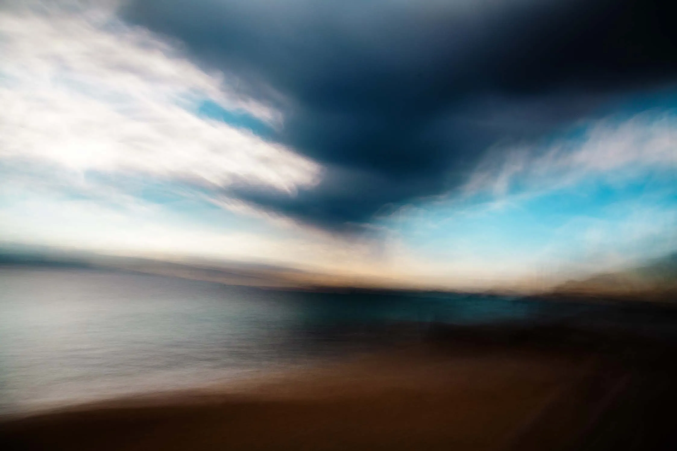 Raggi di sole tra nuvole scure sopra il mare, costa in lontananza.